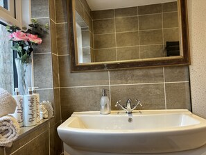 A bathroom with a white sink, a mirror with a decorative frame, and a vase with pink flowers. - House few Mins From Beach With hot tub & Sauna (Shoreham-by-Sea)