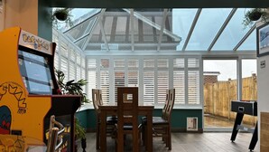 A room with a wooden table and chairs, a Pac-Man arcade machine, and a large window with a view of a brick building. - House few Mins From Beach With hot tub & Sauna (Shoreham-by-Sea)