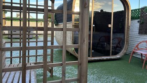 A wooden structure with a glass door, a brick wall, and a green artificial turf area. - House few Mins From Beach With hot tub & Sauna (Shoreham-by-Sea)