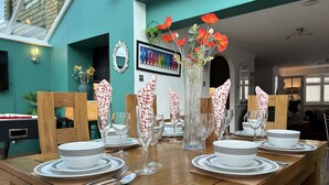 A dining table set with white plates, clear glasses, and red napkins. There is a vase with red flowers and a framed picture on the wall. - House few Mins From Beach With hot tub & Sauna (Shoreham-by-Sea)