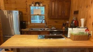 A wooden cabin kitchen with a central island, three bar stools, a refrigerator, and wooden cabinets.