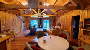 A cozy cabin interior with wooden walls and a high ceiling. There is a fireplace in the background, a round table with chairs, and a bookshelf. - Snowshoe Acres is a beautiful 4 bedroom log cabin (Dunmore)