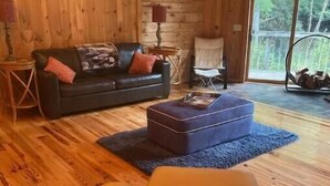 A cozy cabin interior with a leather sofa, a blue ottoman, and a wooden floor.