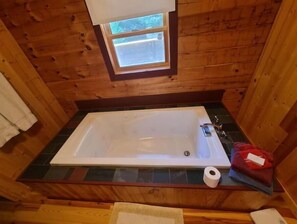 A wooden cabin bathroom with a bathtub, a window, and a towel on the floor. - Snowshoe Acres is a beautiful 4 bedroom log cabin (Dunmore)