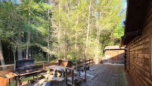 A wooden deck with a grill, picnic table, and outdoor seating area surrounded by trees.