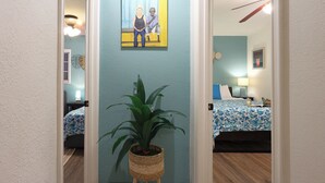 A hallway with a potted plant, a painting of two people, and a bed with a blue floral bedspread. - Stylish 2B2B Hideaway 10 mins. drive to Disneyland (Santa Ana)