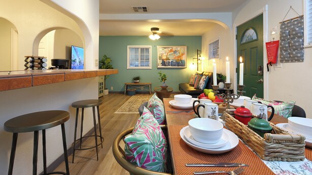 A dining area with a wooden table set for a meal, a bar with stools, and a green door in the background. - Stylish 2B2B Hideaway 10 mins. drive to Disneyland (Santa Ana)