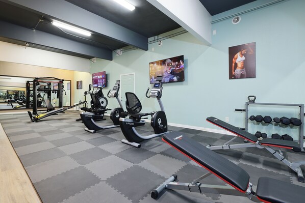 A gym with cardio machines, weightlifting equipment, and a mirror.