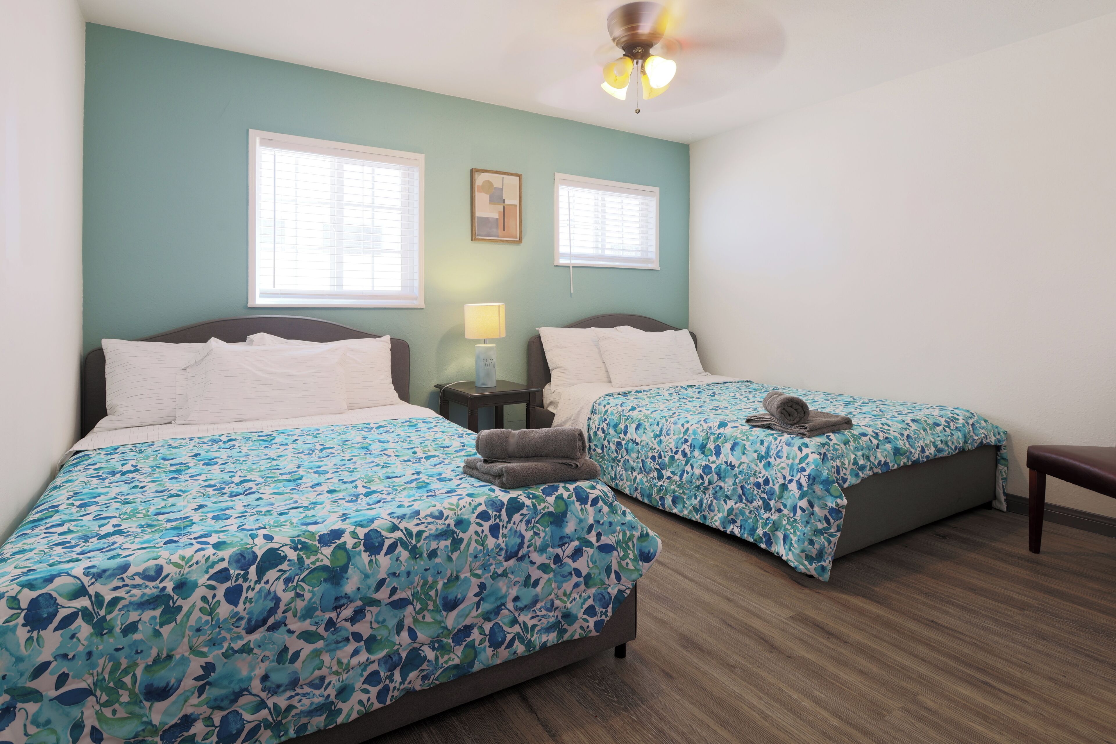 A hotel room with two beds, a ceiling fan, and a nightstand with a lamp.