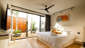 Ein modernes Schlafzimmer mit einem großen Bett, einem Deckenventilator und Blick ins Freie.