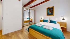 A bedroom with a wooden bed, teal bedding, a large mirror, and bedside lamps. - La Renaissance Moderne (Kaysersberg)