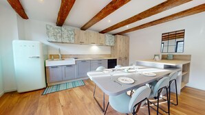 A modern kitchen with wooden beams, a built-in fridge, and a dining area with a table set for four. - La Renaissance Moderne (Kaysersberg)