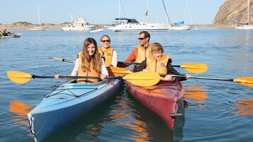 A group of people in kayaks on calm water with boats in the background.
