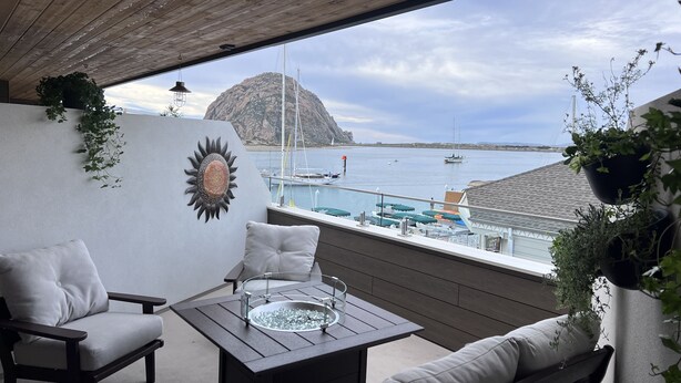 A balcony with a view of the sea, featuring a table, chairs, and potted plants. - HarborWalk Inn (Morro Bay)
