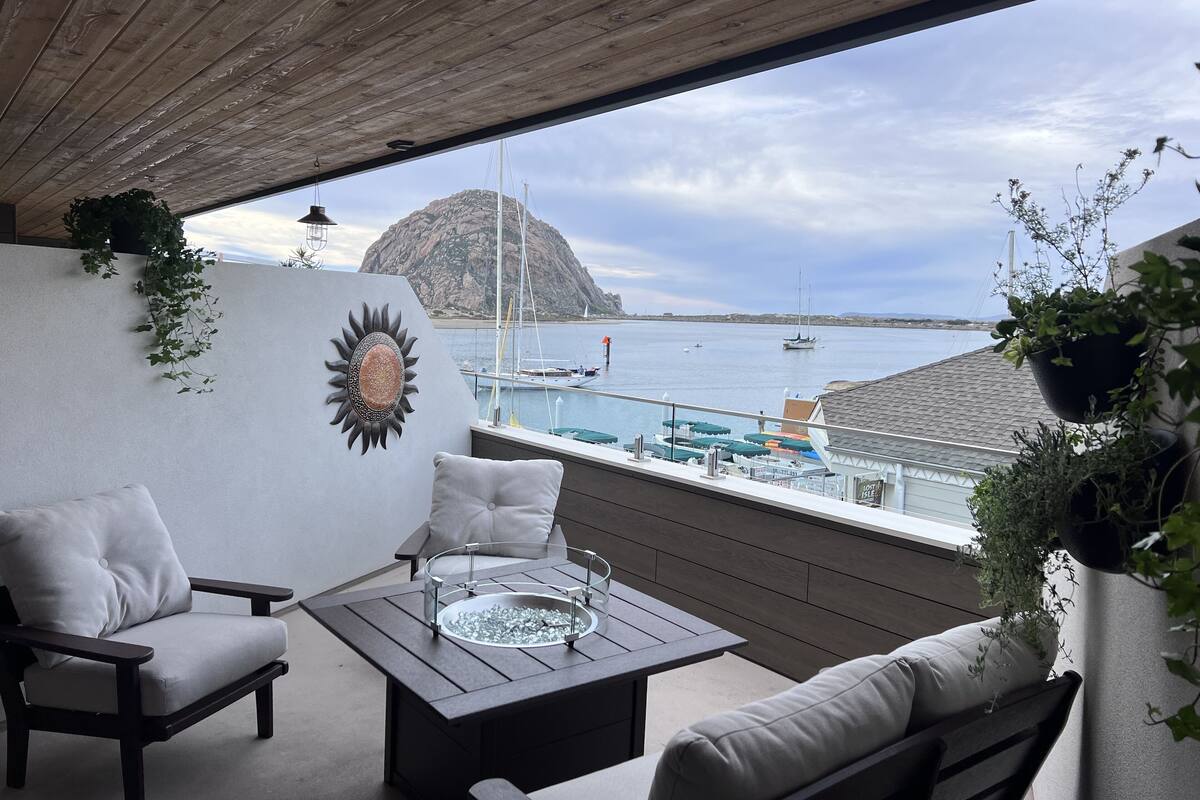 Un balcón con vistas al mar, que incluye una mesa, sillas y plantas en macetas.