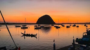 A marina at sunset with boats docked, a prominent hill in the background, and calm waters reflecting the sky. - HarborWalk Inn (Morro Bay)