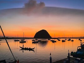 Un puerto deportivo al atardecer con barcos amarrados, una colina destacada al fondo y aguas tranquilas que reflejan el cielo.