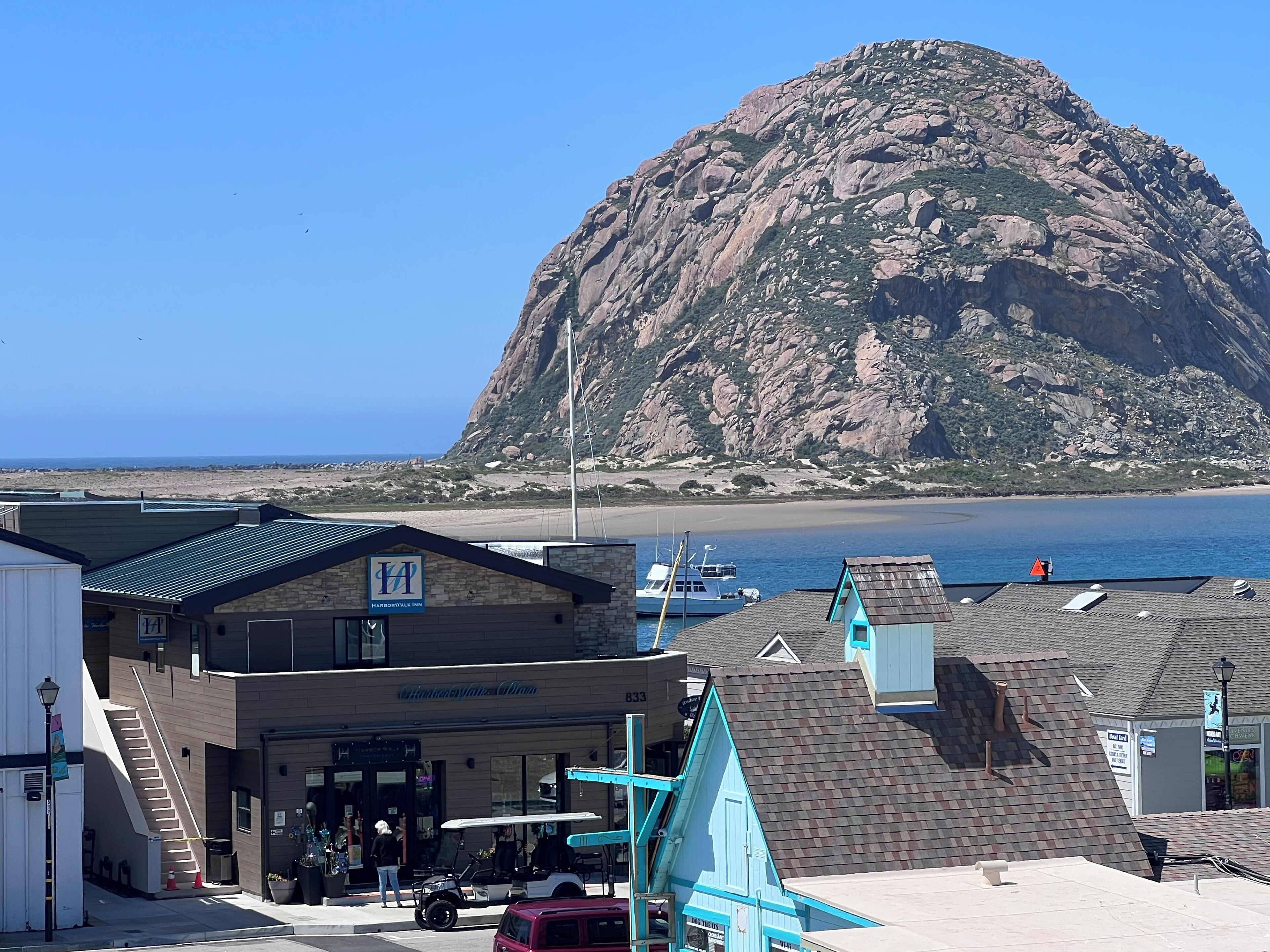 A coastal hotel with a view of the sea and a prominent rocky hill in the background.