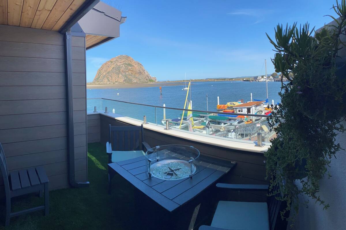 Un balcón con mesa y sillas, con vistas a una marina llena de barcos y una isla rocosa a lo lejos.