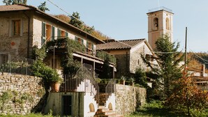 A stone building with a bell tower, a staircase leading to a balcony, and a surrounding garden.