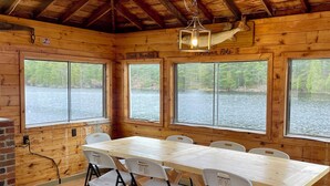 A wooden cabin with a large dining table, chairs, and a small round table.