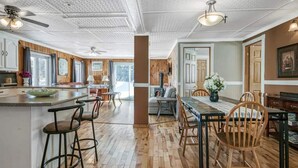 A spacious kitchen with wooden flooring, a central island with stools, and a dining area with a wooden table and chairs.