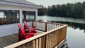 A wooden deck with a railing, a building with large windows, and a calm lake in the background.