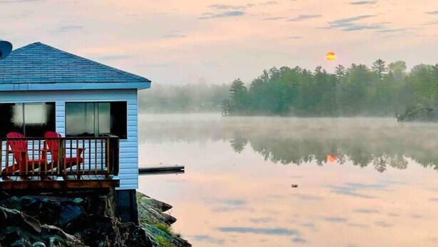 A cabin with a dock extending into a calm lake, surrounded by trees and mist.