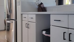 A modern kitchen with white cabinetry, a stainless steel refrigerator, a trash bin, and a knife block. - Old Town Scottsdale modern decor big pool hot tub TV on patio Comfort Convenient (Scottsdale)