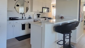 A modern kitchen with white cabinetry, a central island with bar stools, a round mirror, and pendant lighting. - Old Town Scottsdale modern decor big pool hot tub TV on patio Comfort Convenient (Scottsdale)