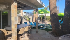 An outdoor patio with a pool, stone pillars, wicker chairs, and umbrellas. - Old Town Scottsdale modern decor big pool hot tub TV on patio Comfort Convenient (Scottsdale)