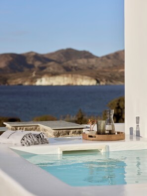 Ein Poolbereich mit Blick auf das Meer und die Berge, ein Handtuch und eine Ablage mit einer Vase und einer Kerze.