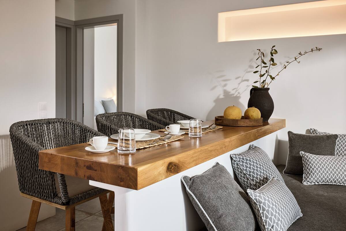 A dining area with a wooden table, wicker chairs, and a vase with branches.