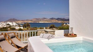 A balcony with a hot tub, lounge chairs, and a view of the sea and mountains. - Manesis Suites (Milos)