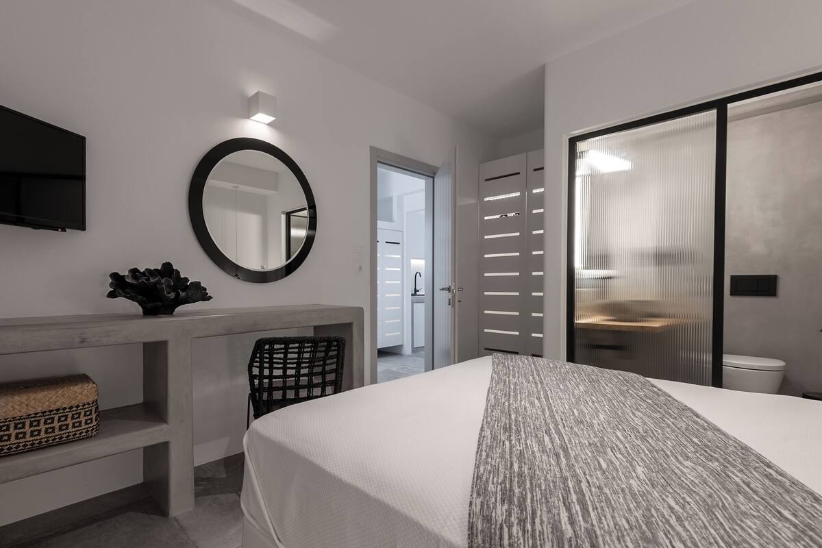A modern bedroom with a bed, a bedside table, a mirror, and a TV.