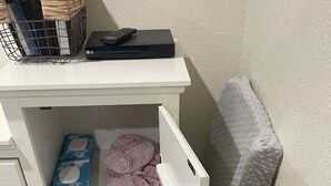 Un contenedor de almacenamiento blanco con un colchón, una cesta y un mando a distancia.