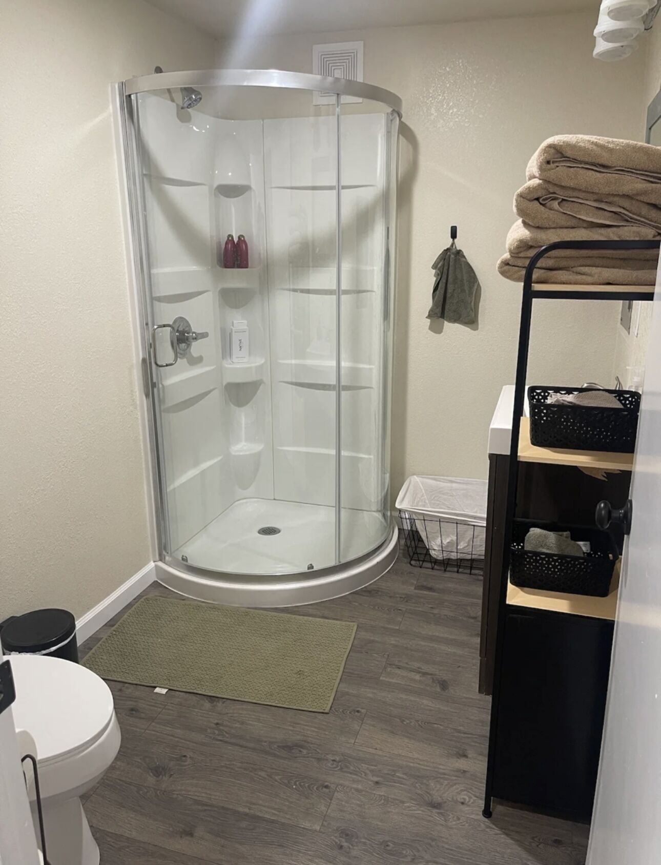 A bathroom with a glass shower enclosure, a toilet, a sink, and a shelf with towels.