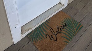 Una puerta blanca con teclado numérico y un felpudo que dice 'Welcome'.