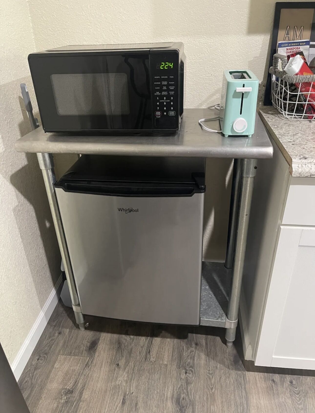 A compact kitchenette with a black microwave, a toaster, and a Whirlpool refrigerator.