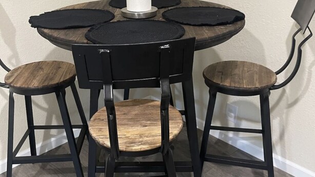 Una mesa de comedor redonda con cuatro sillas, cada una con asiento de madera y estructura de metal negro.