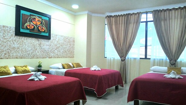 A hotel room with three beds, each with a red bedspread and white pillows. There is a painting on the wall above the beds, a window with curtains, and a small plant on the nightstand. - Hotel Vanderkris Chone (Chone)