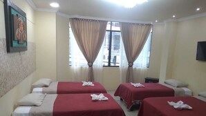 A hotel room with four beds, each with a red bedspread and a white towel. There are beige curtains on the windows, and a painting on the wall. - Hotel Vanderkris Chone (Chone)