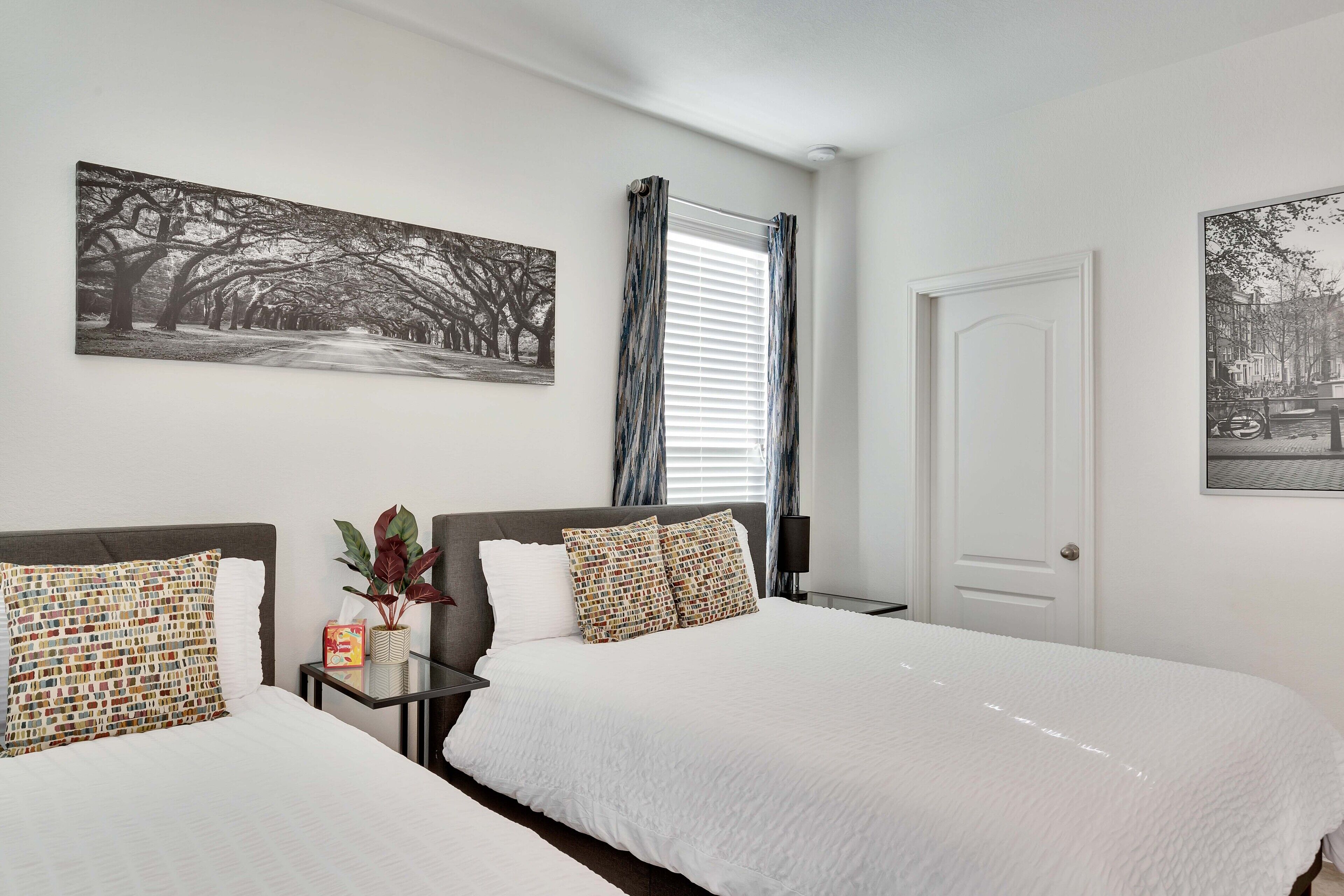 A hotel room with two beds, a large window with curtains, and artwork on the walls.