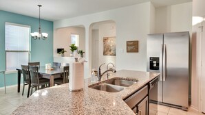 Cozinha moderna com bancadas de granito, eletrodomésticos de aço inoxidável e uma área de jantar com mesa e cadeiras.