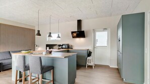 Una cocina moderna con una isla central, taburetes de bar, una zona de comedor con sofá y un ventanal grande.