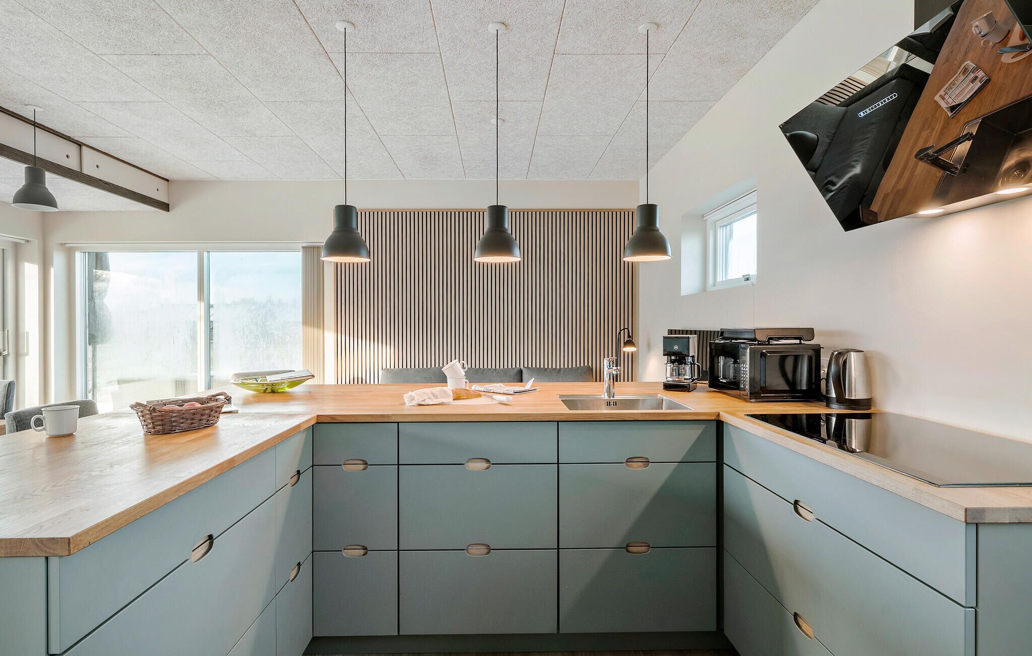 Een moderne keuken met een centraal eiland, hangende lampen en uitzicht op de omgeving.