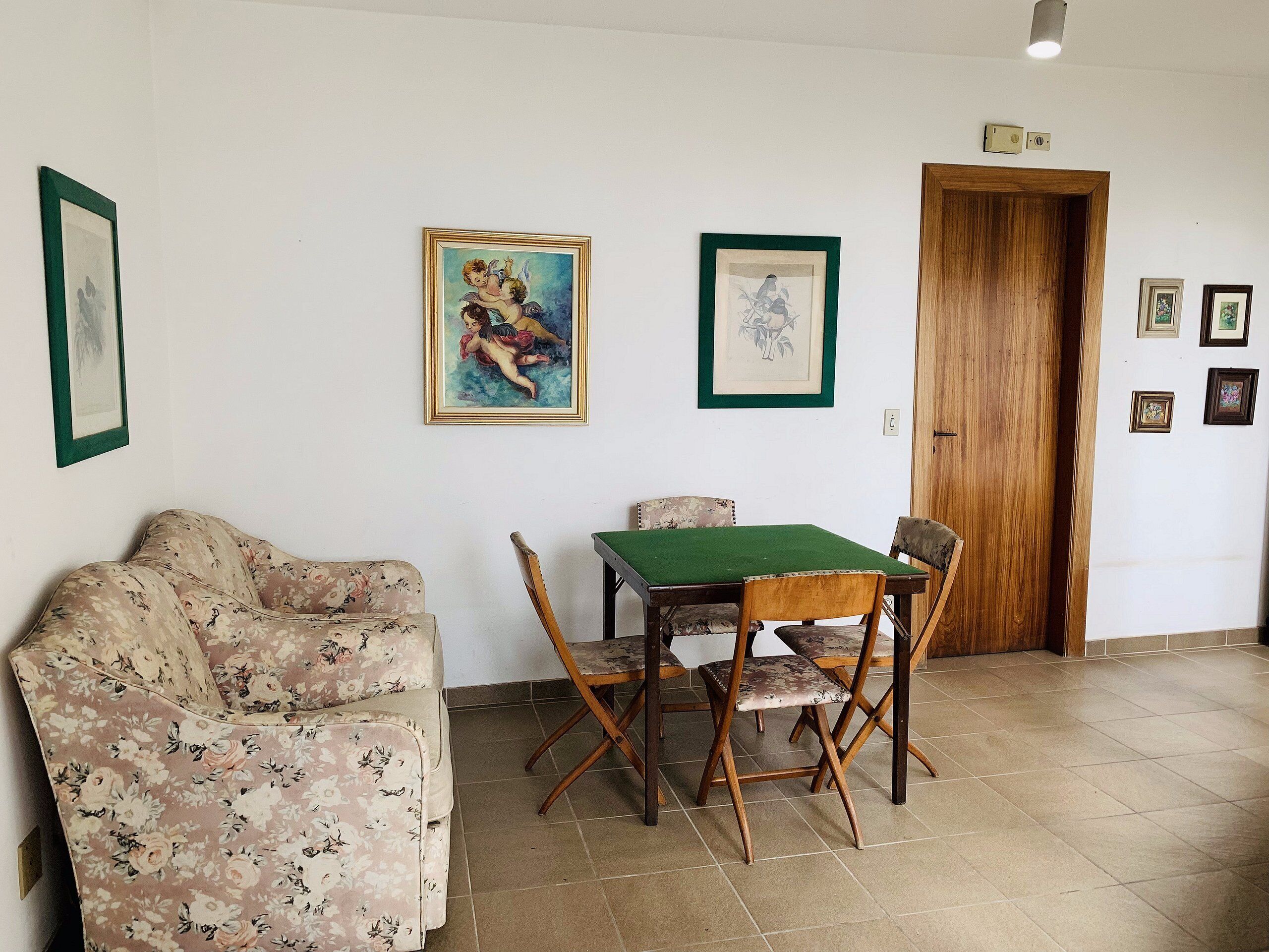 Una stanza con un divano floreale, un tavolo da pranzo in legno con tovaglia verde e opere d'arte incorniciate alle pareti.
