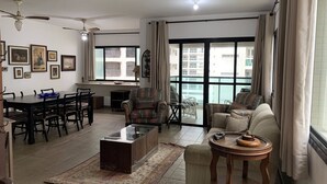 Un salón amplio con comedor, ventanas grandes con cortinas, un ventilador de techo y varias fotografías enmarcadas en las paredes.