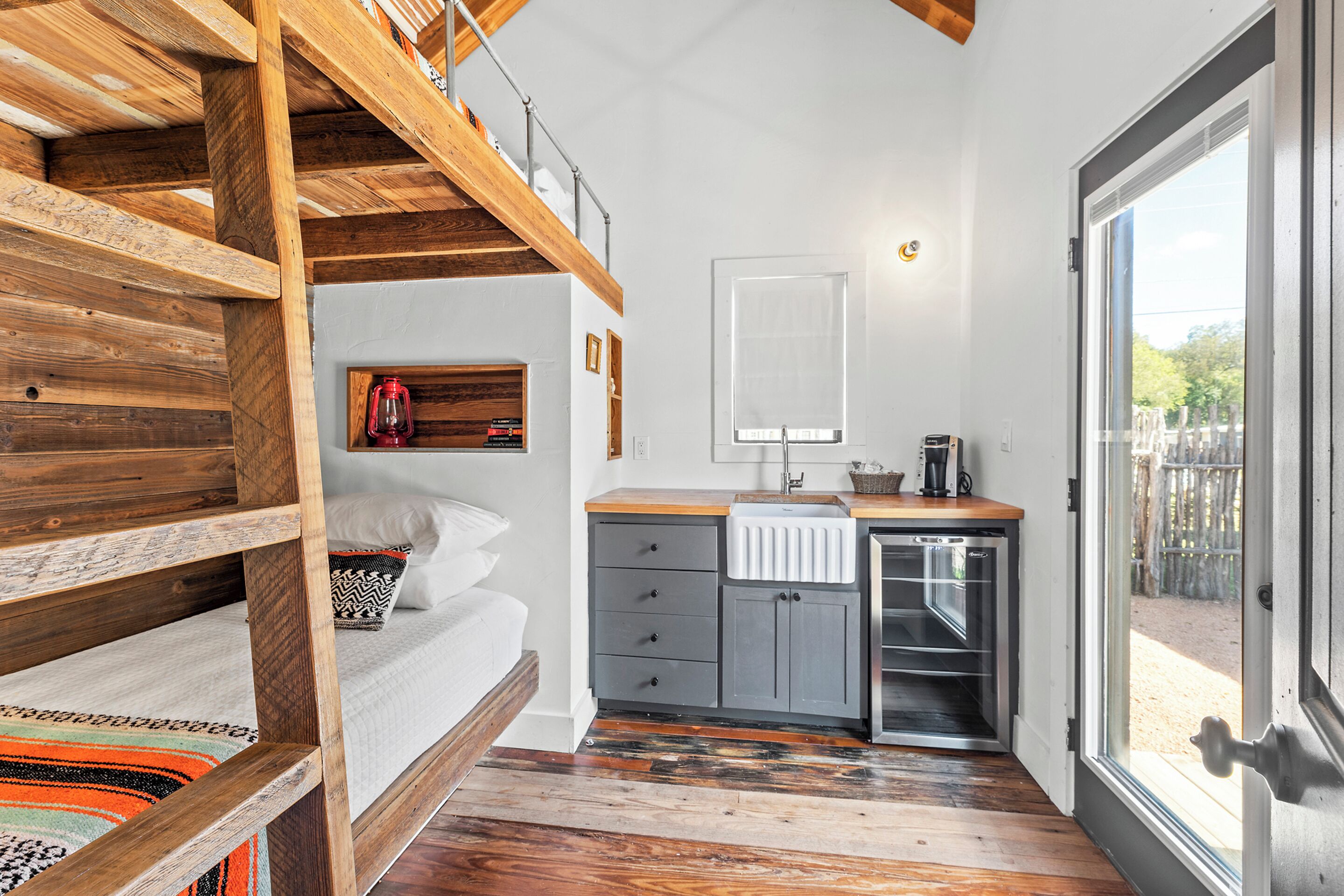 A compact bedroom with a bunk bed, a small bedside table with a lantern, and a window with a view of the outside.