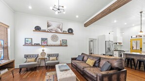 A modern living room with a sofa, chairs, a coffee table, and a kitchen area with a refrigerator and a yellow door. - Luxury 3 Bedroom House with Airstream, Cabin, Private Fireplace, and Plunge Pool (Comfort)